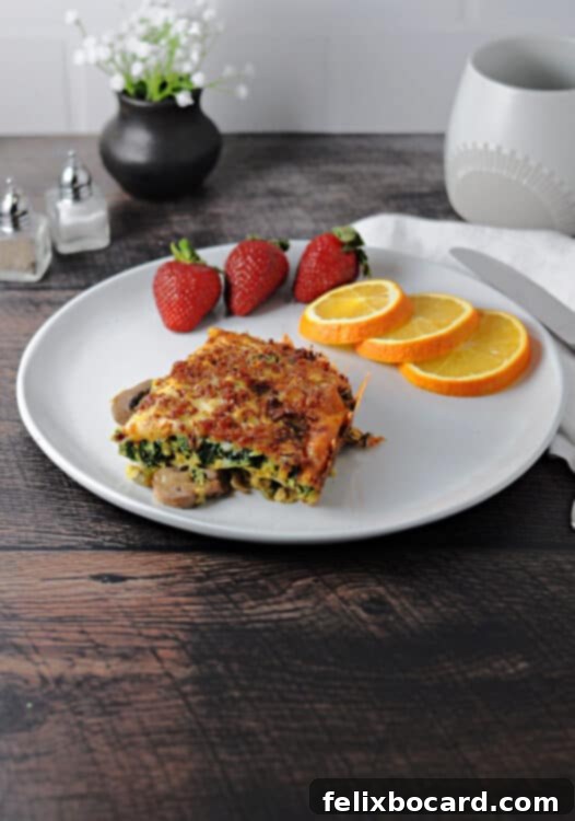 Keto Breakfast Casserole with Spinach, Bacon, and Eggs 8 square of low carb breakfast casserole on a white plate with fresh fruit