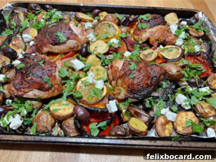 Close-up of Mediterranean chicken and vegetables roasting on a sheet pan, showcasing golden-brown chicken thighs, caramelized onions and peppers, and tender baby potatoes. Garnished with fresh herbs and crumbled feta cheese.