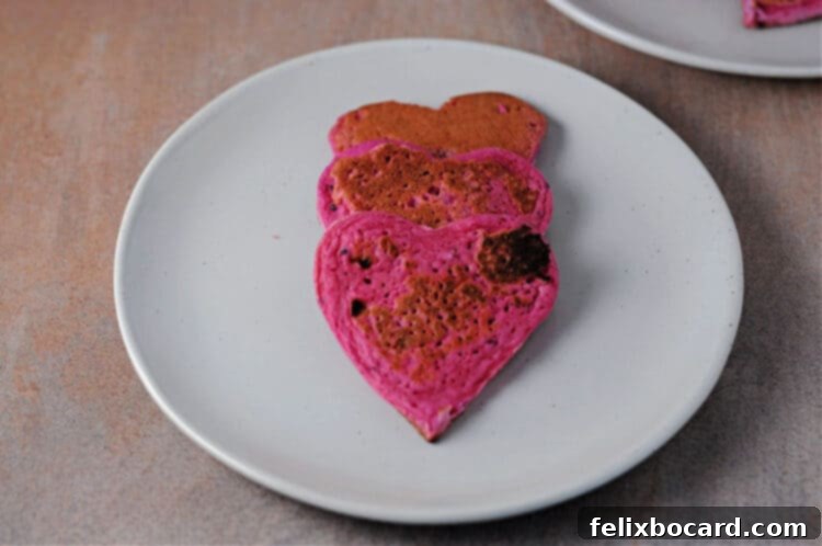 A charming close-up of three heart-shaped dragon fruit pancakes elegantly arranged on a small white plate, ready for a delightful breakfast