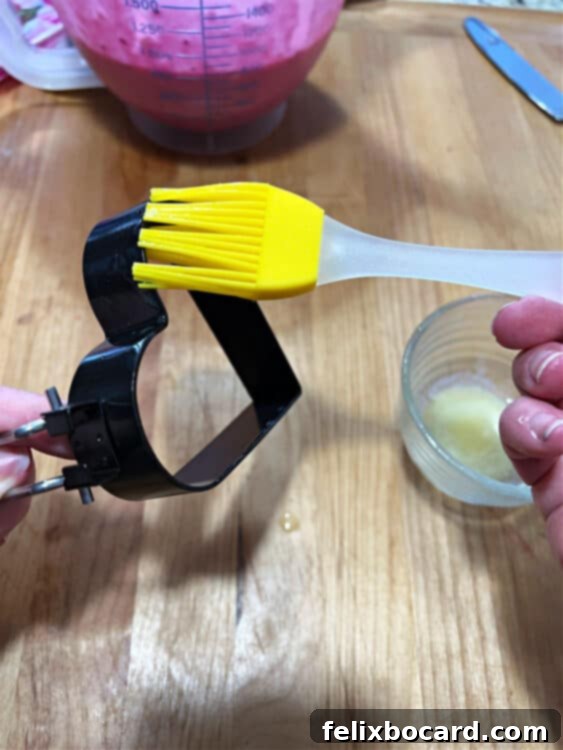 A close-up of a heart-shaped egg mold being thoroughly greased with cooking spray before making dragon fruit pancakes