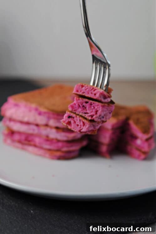 A fork holding a fluffy bite of a heart-shaped dragon fruit pancake, showing its enticing texture and color