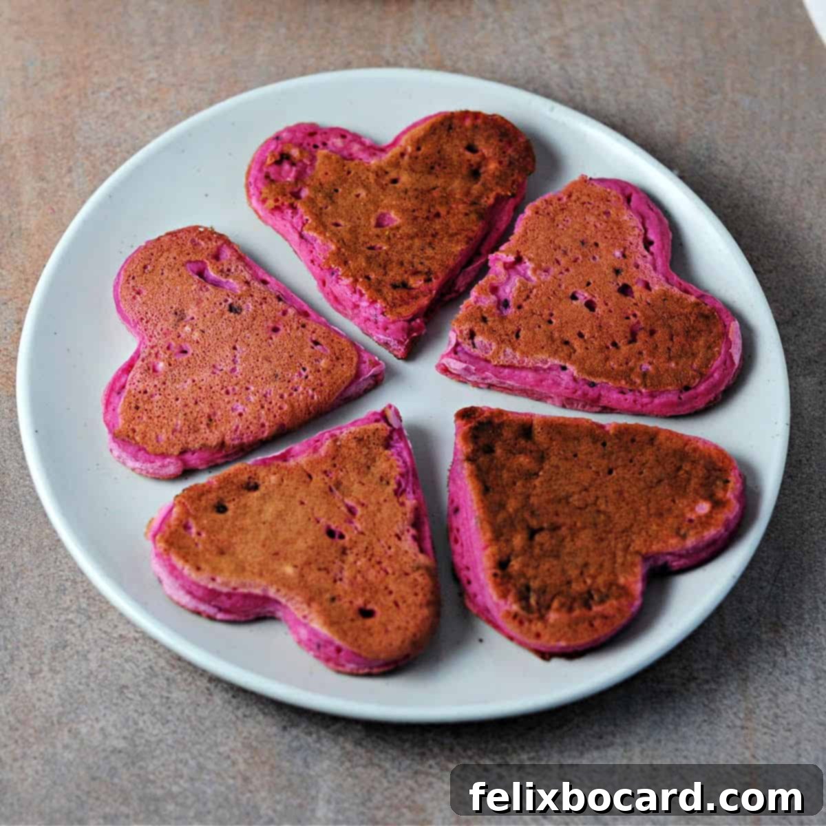 A stunning overhead shot of five heart-shaped dragon fruit pancakes beautifully stacked on a small white plate, ready for serving