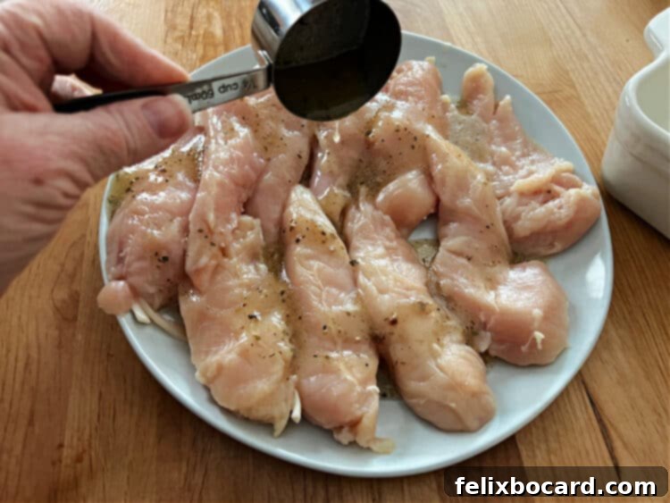 Mediterranean Feta Chicken Tenders 4 Chicken tenderloins being drizzled with Greek dressing on a plate, ready for baking.