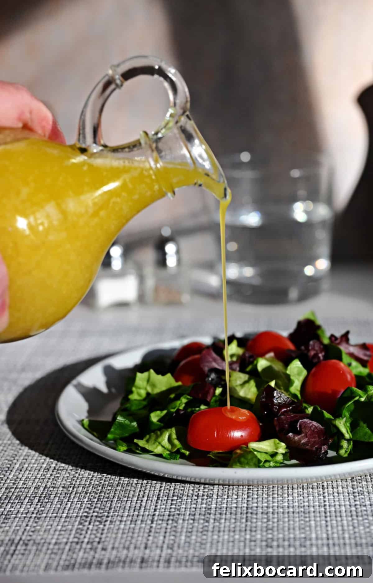 Cruet of Meyer lemon vinaigrette pouring onto a green salad.