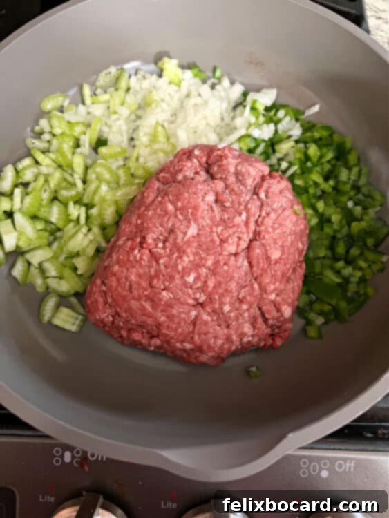 Raw ground beef and chopped vegetables, including onion, green pepper, and celery, are being added to a hot skillet, ready for browning.