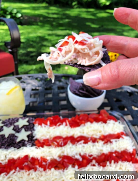 hand holding a chip covered in dip with whole pan of taco dip behind and outdoors
