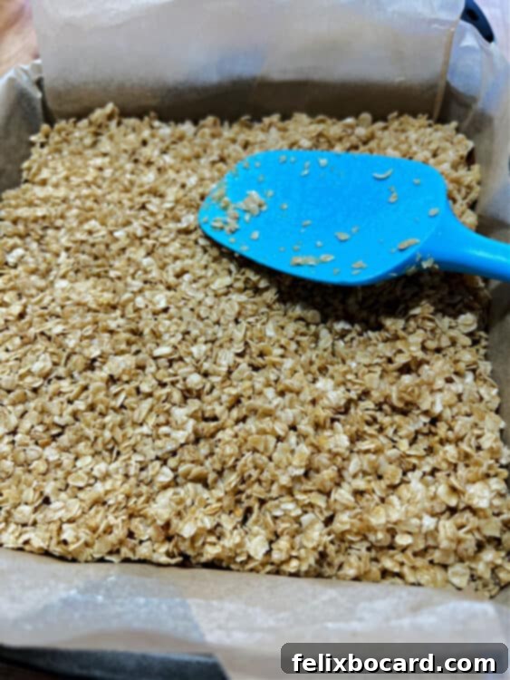 A spatula gently patting the sprinkled oat topping onto the chocolate layer, ensuring it adheres lightly.