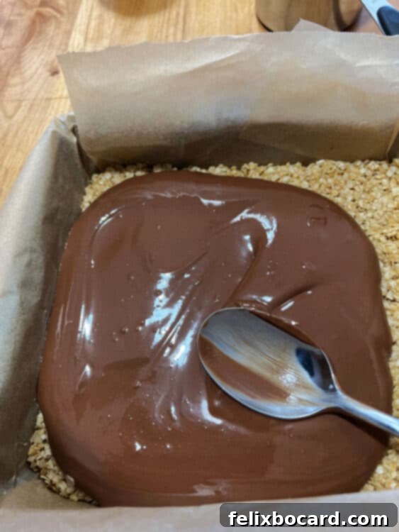 Smooth chocolate-peanut butter mixture being spread evenly over the oatmeal crust in a pan with a spatula.