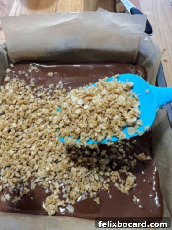 The reserved oat mixture being sprinkled over the chocolate-peanut butter layer in the pan.