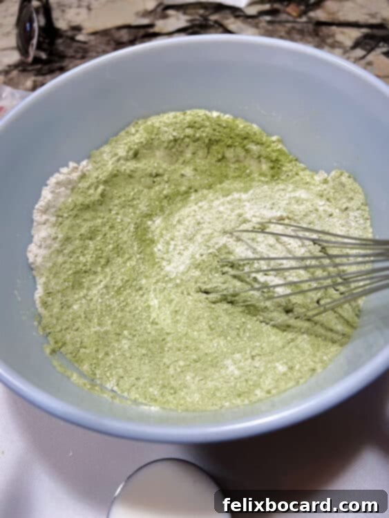 Dry ingredients, including flour, baking powder, baking soda, salt, and matcha powder, being whisked together in a ceramic bowl until evenly combined.