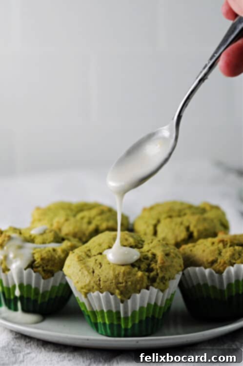 Lemon powdered sugar glaze being drizzled from a spoon onto the top of a cooled matcha green tea muffin, adding a glossy finish.