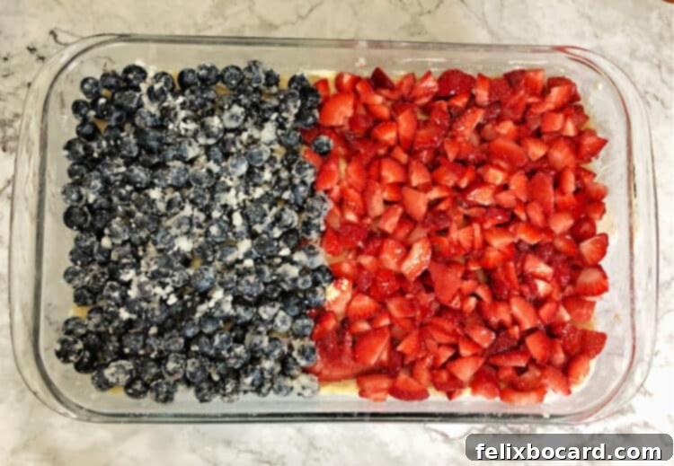 Star Spangled Berry Crumble Bars 2 Top-down view of a 9x13 inch baking pan, half-layered with fresh blueberries and the other half with fresh, sliced strawberries.