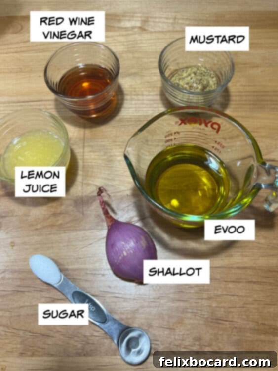 A selection of fresh ingredients for red wine shallot vinaigrette: red wine vinegar, grainy mustard, extra virgin olive oil, a fresh shallot, lemon, and sugar cubes, arranged artfully on a light background.