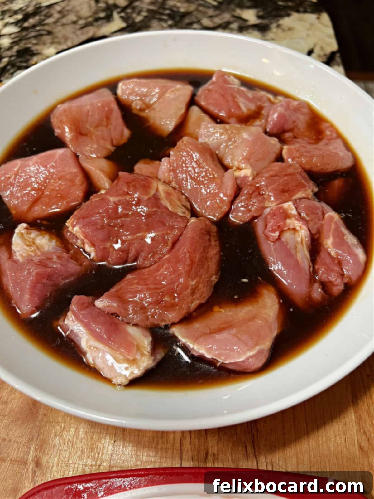 Cubes of pork marinating in a bowl with soy sauce and sherry.