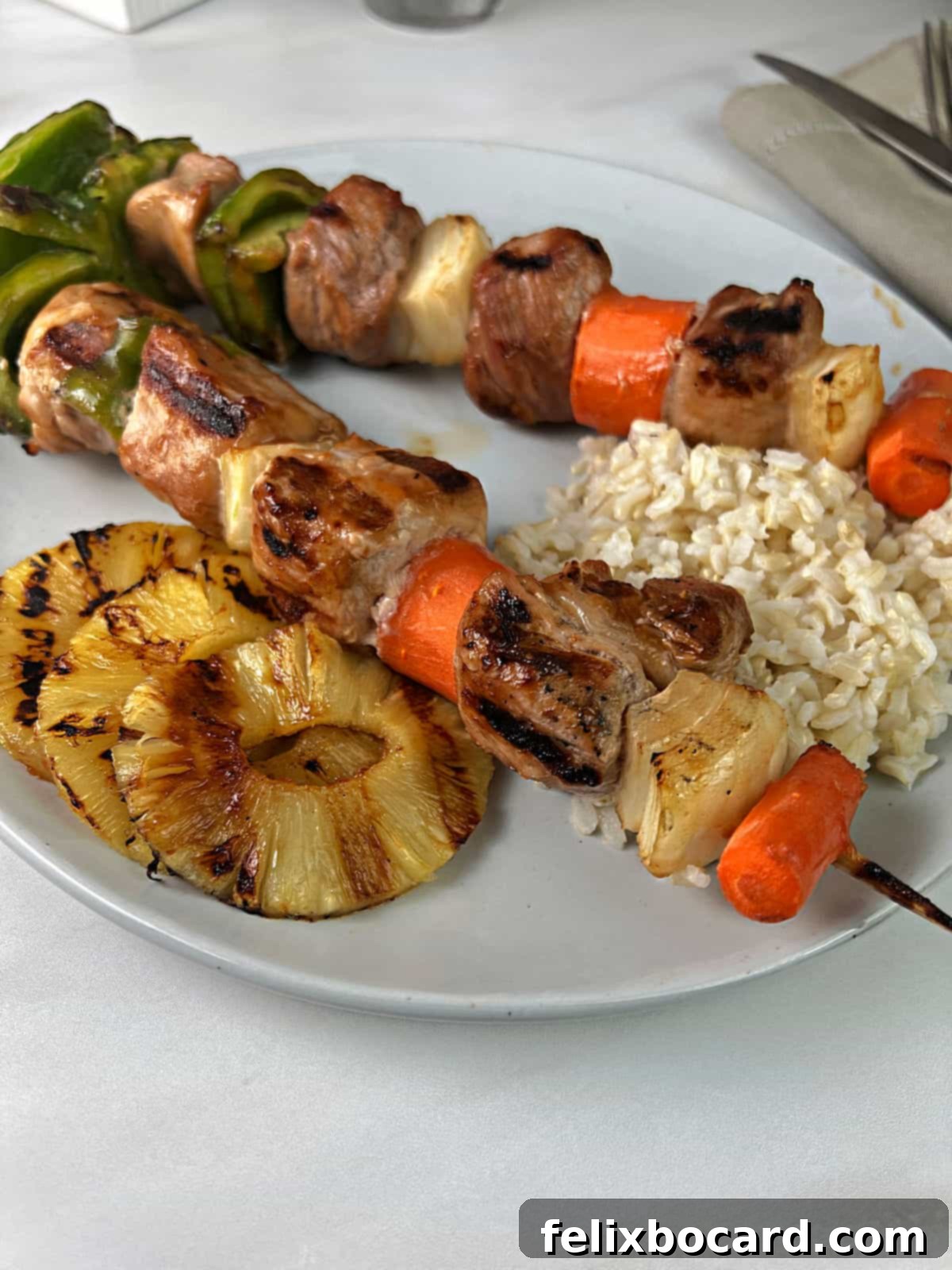 Two sweet and sour pork kabobs served with rice and grilled pineapple slices.