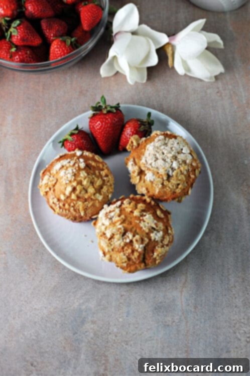 Three strawberry Greek yogurt muffins on a plate with fresh strawberries.