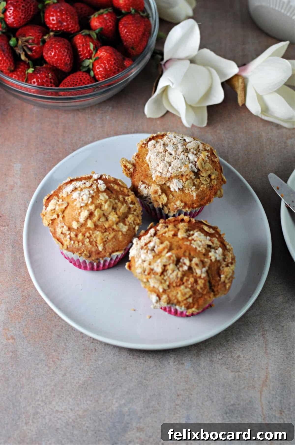 Three strawberry yogurt muffins on a small plate, beautifully arranged.