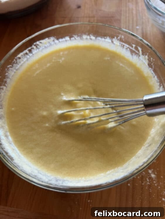 A whisk mixing wet ingredients (eggs, Greek yogurt, oil, vanilla) in a bowl.