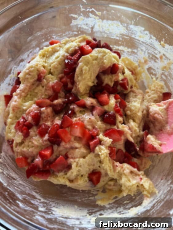 Strawberries being gently mixed into the muffin batter with a spatula.
