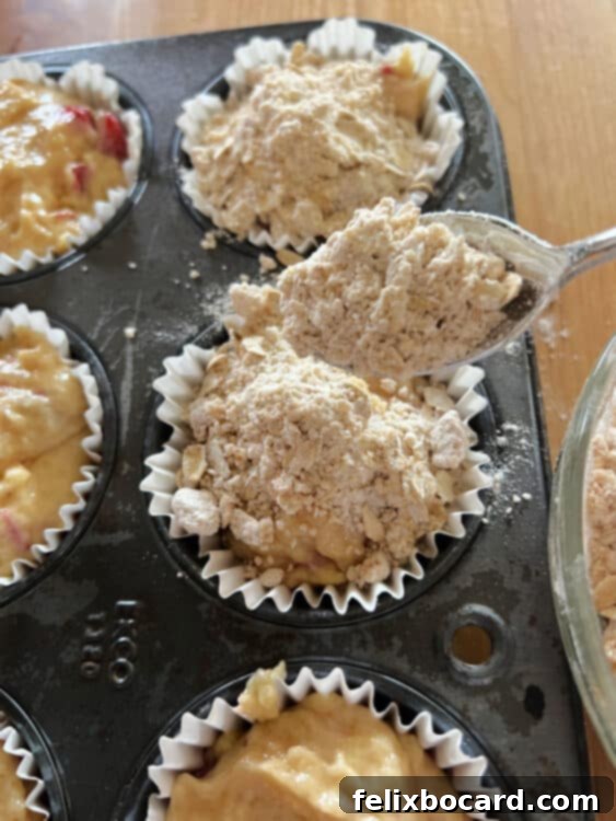 Streusel being sprinkled on top of unbaked muffins in a muffin tin.