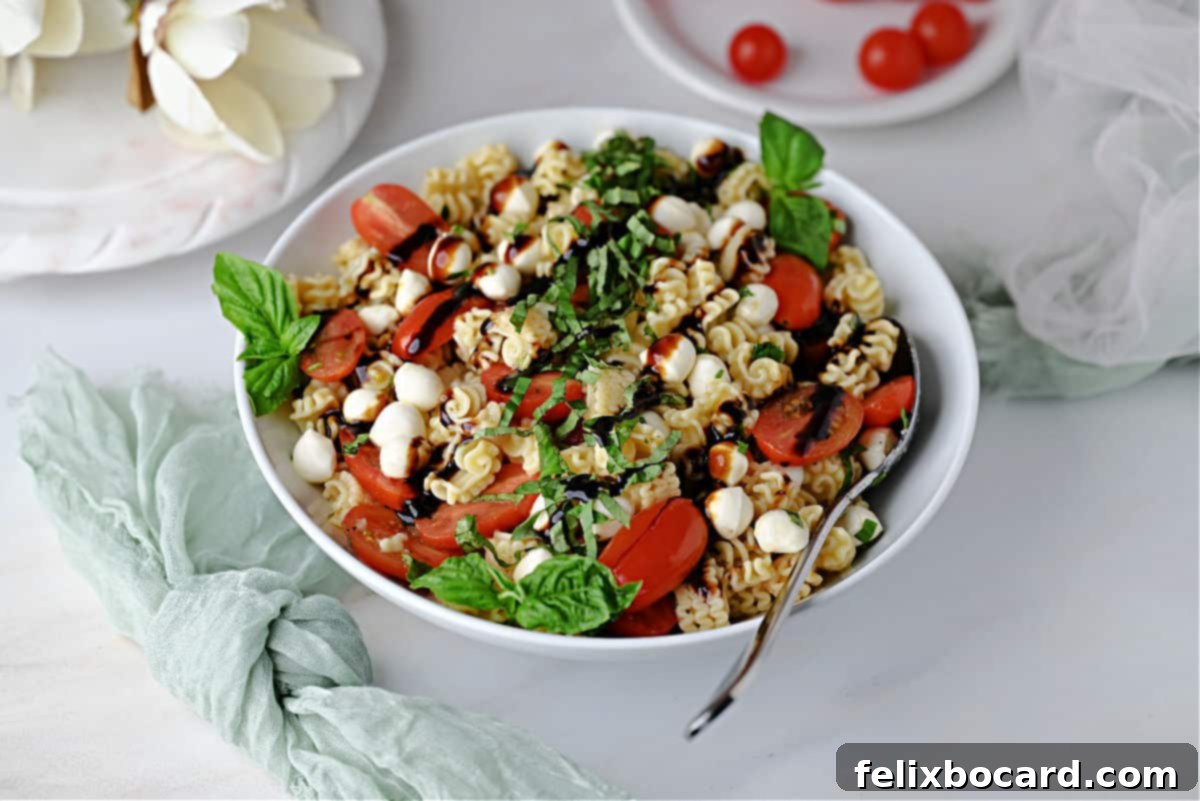 Bowl of Caprese pasta salad ready to serve, garnished with fresh basil and balsamic glaze.
