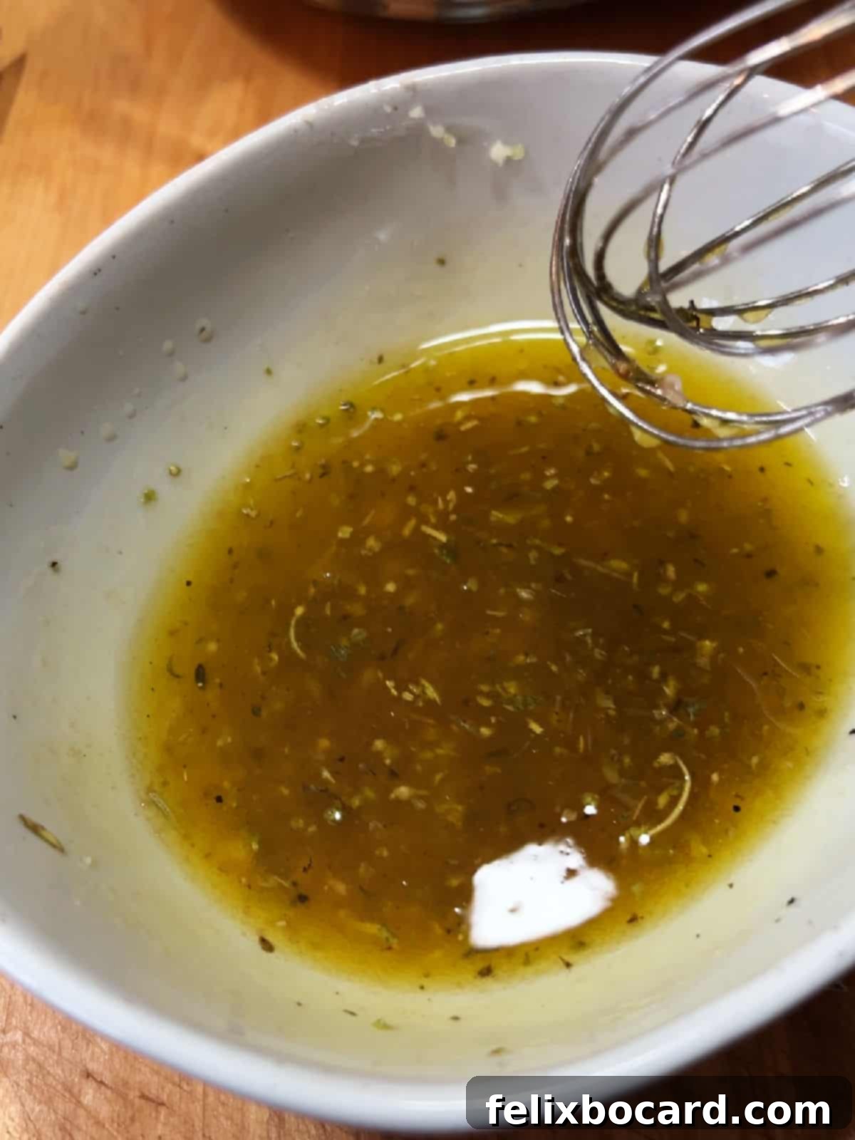 Close-up of dressing ingredients being whisked together in a small bowl.