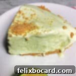 A vibrant slice of frozen tropical lime pie on a white plate, showcasing its creamy green filling and golden crust, garnished with a lime wedge.