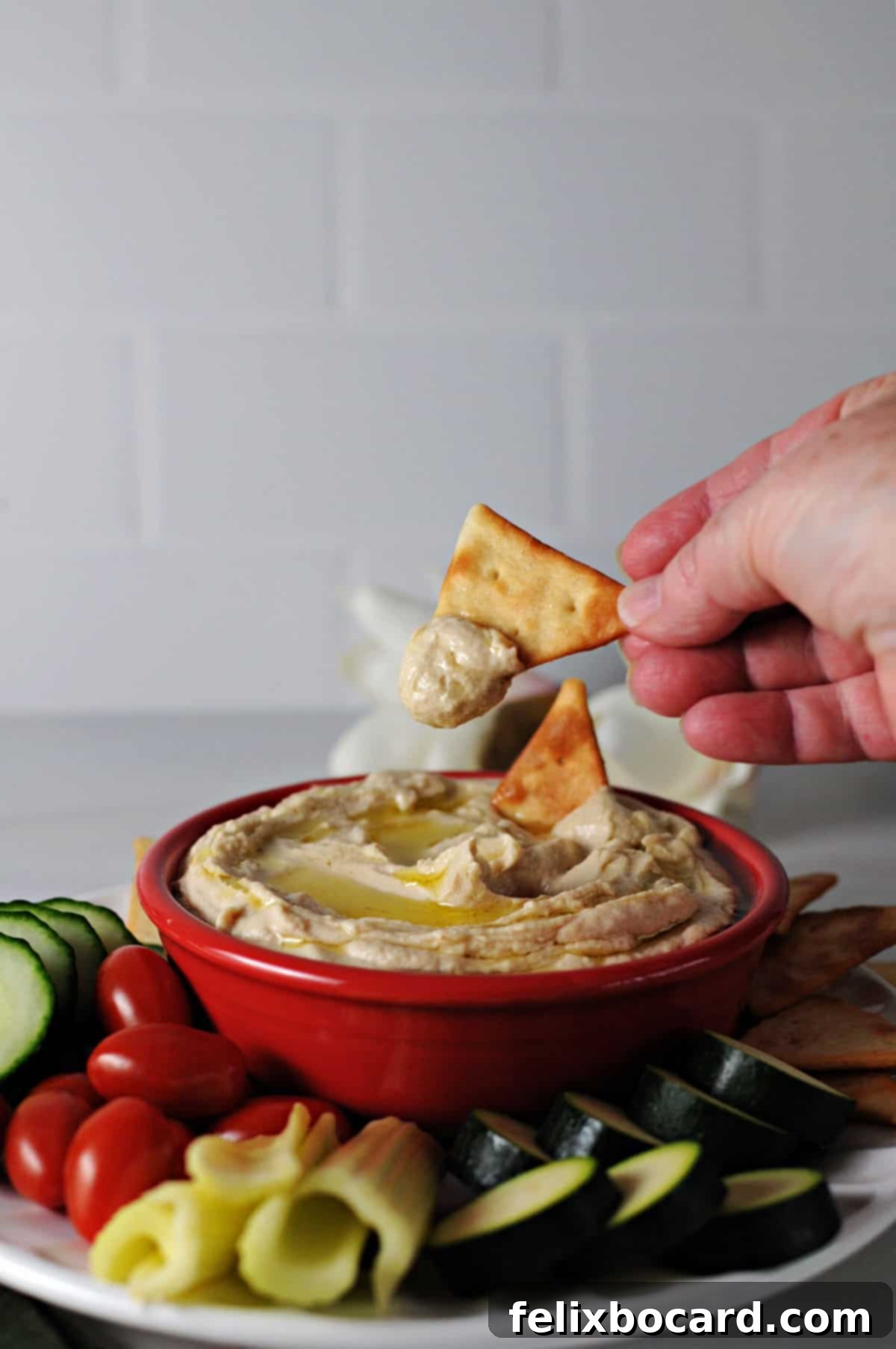 Hand holding a cracker dipping into a bowl of creamy butter bean hummus.