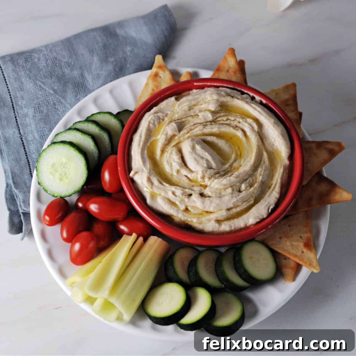 Bowl of buttery smooth butter bean hummus surrounded by an assortment of crackers and fresh vegetables.