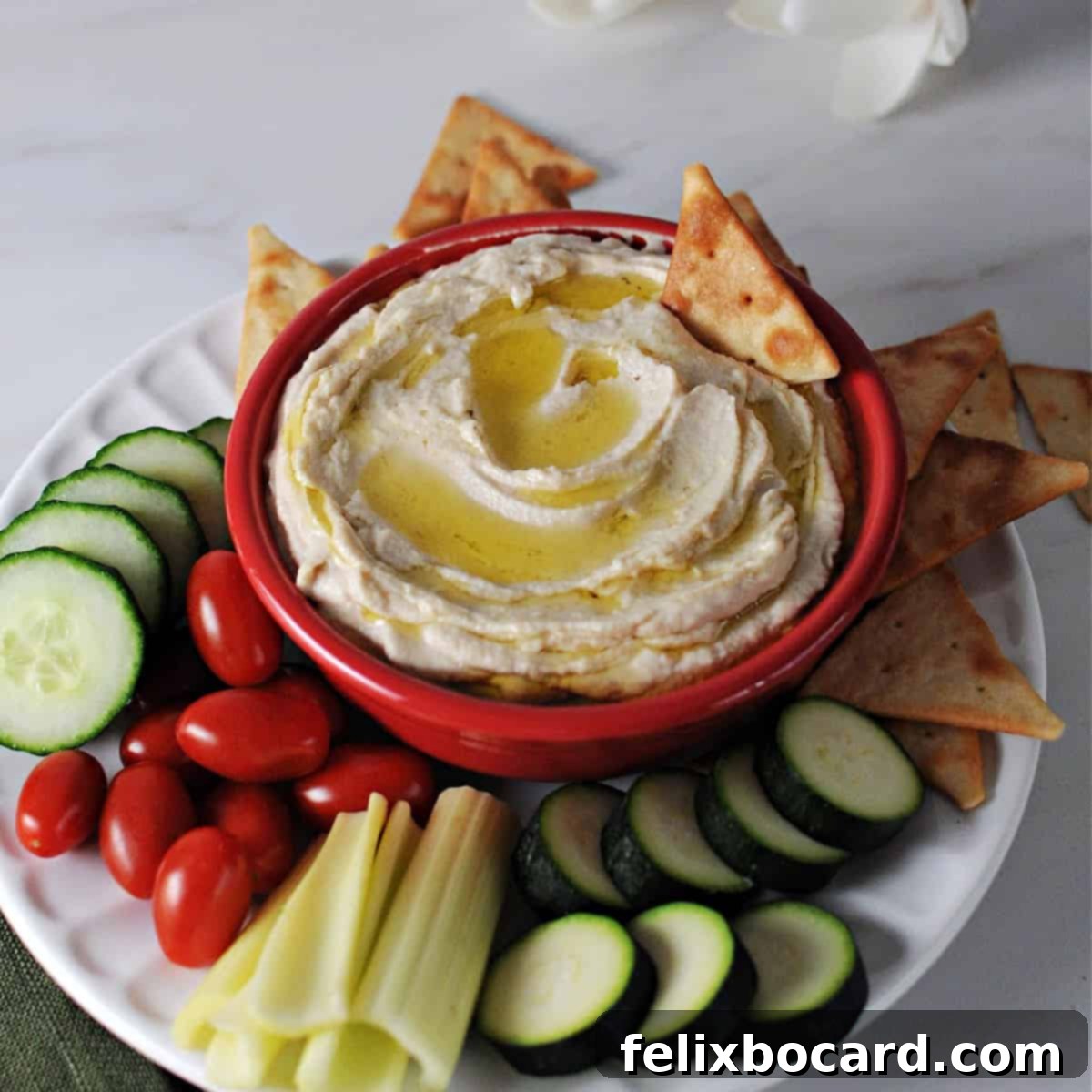 Butter bean hummus in a red bowl surrounded by crackers and fresh vegetables, ready to serve.
