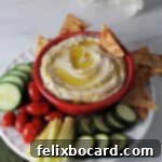 Butter bean hummus in a red bowl surrounded by crackers and veggies.