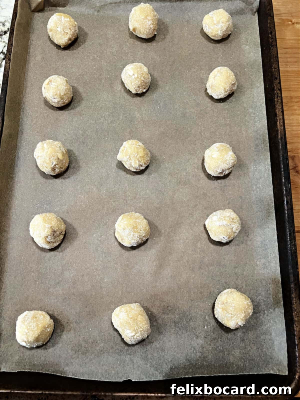 Balls of oatmeal coconut cookie dough lined up on a baking sheet, coated in sugar.