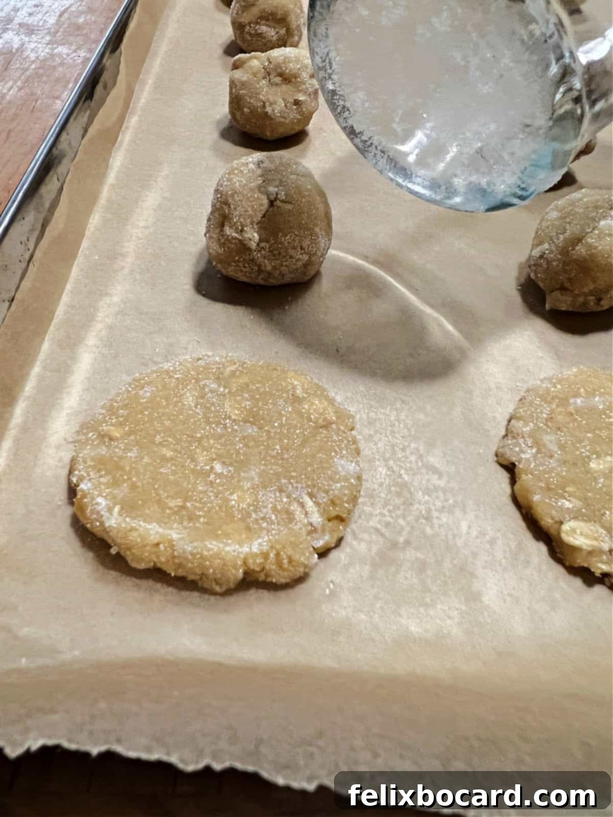 Flattened oatmeal coconut cookie dough with a sugar-dipped glass being lifted away.