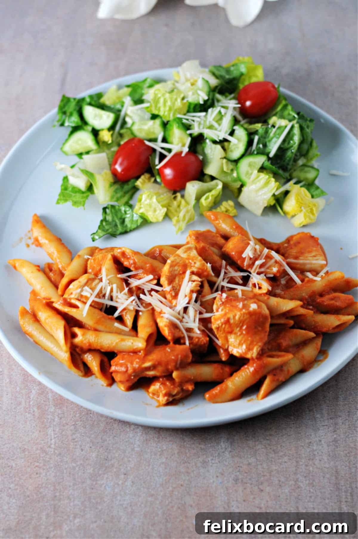 A vibrant plate of penne alla vodka with tender chicken pieces, artfully arranged beside a fresh green salad.