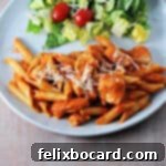 A beautifully plated dish of creamy penne alla vodka with tender chicken, garnished with fresh herbs, alongside a small side salad.