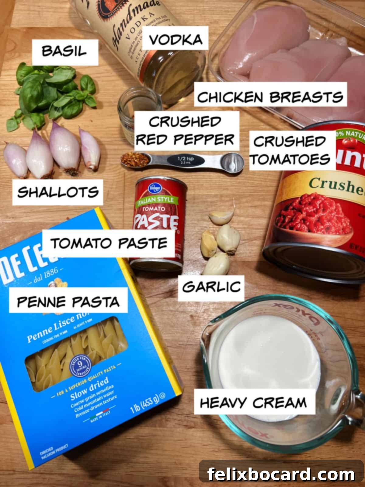 A flat lay of fresh ingredients for penne alla vodka: vodka, chicken breasts, crushed tomatoes, red pepper flakes, heavy cream, garlic cloves, tomato paste, penne pasta, shallots, and fresh basil leaves.