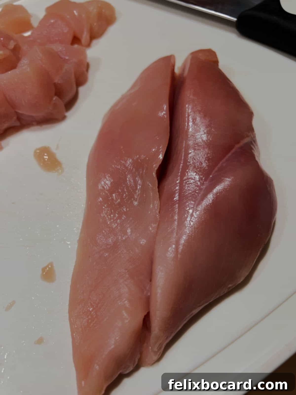 Chef's hand carefully slicing a raw chicken breast lengthwise on a cutting board, preparing it for a recipe.