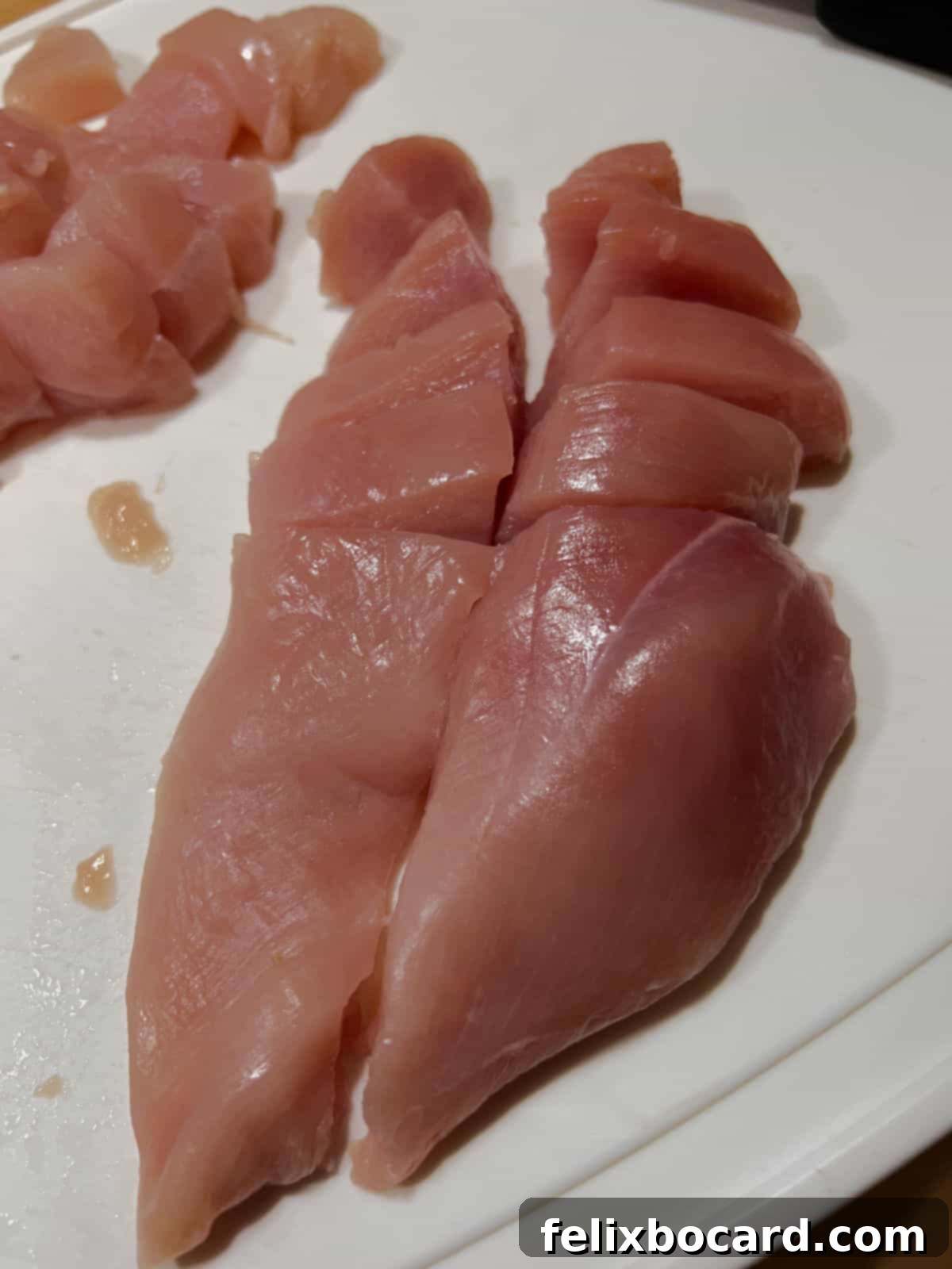 Close-up of chicken breast pieces cut crosswise against the grain, ready for cooking, on a wooden cutting board.