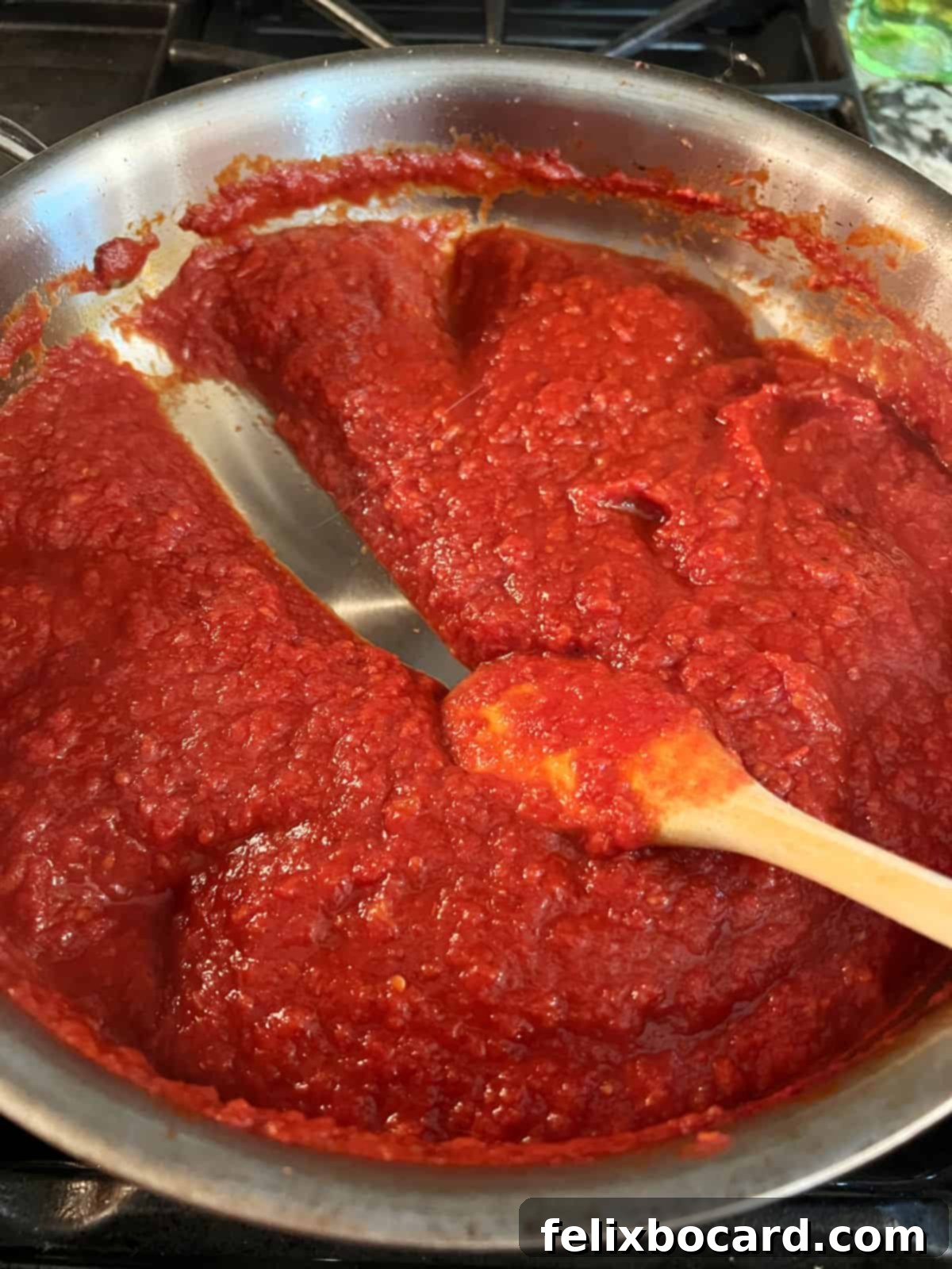 Close-up of creamy red tomato sauce simmering and thickening in a large skillet, indicating the development of rich flavors.