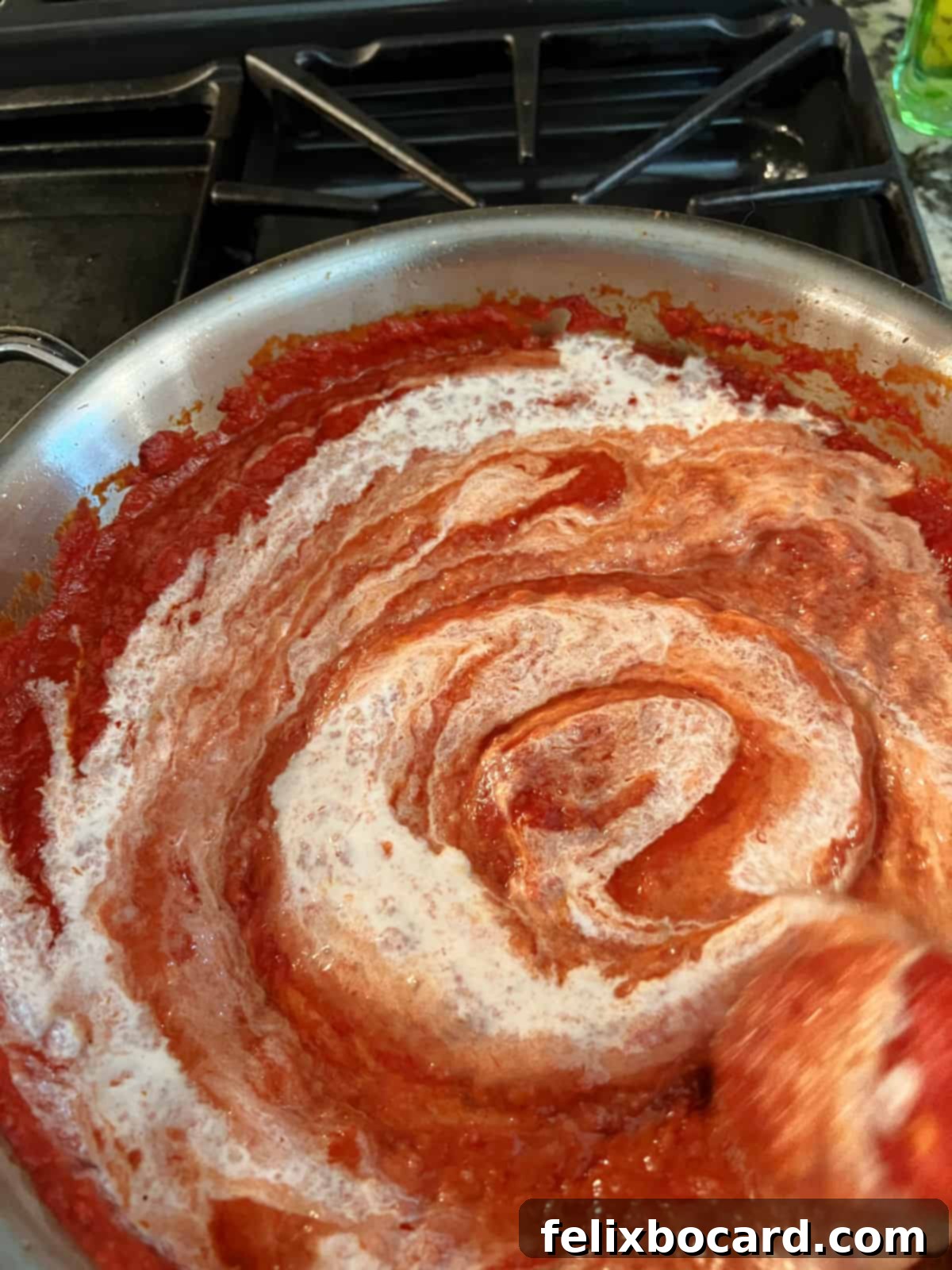 A luscious stream of heavy cream being stirred into a simmering tomato sauce in a skillet, creating a creamy vodka sauce.