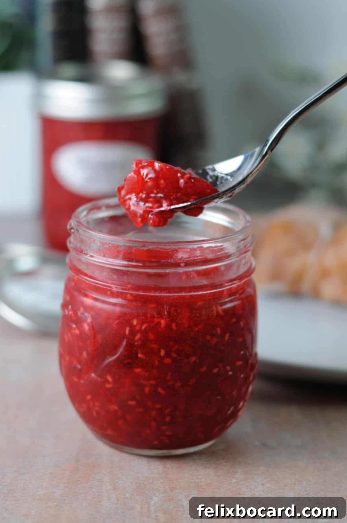 spoon of raspberry freezer jam held above a full jar of jam.