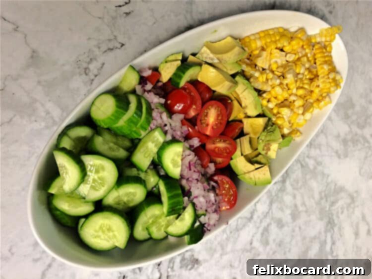 Bowl of separate ingredients: corn, avocado, tomatoes, onion, cucumber, ready for a delicious salad.