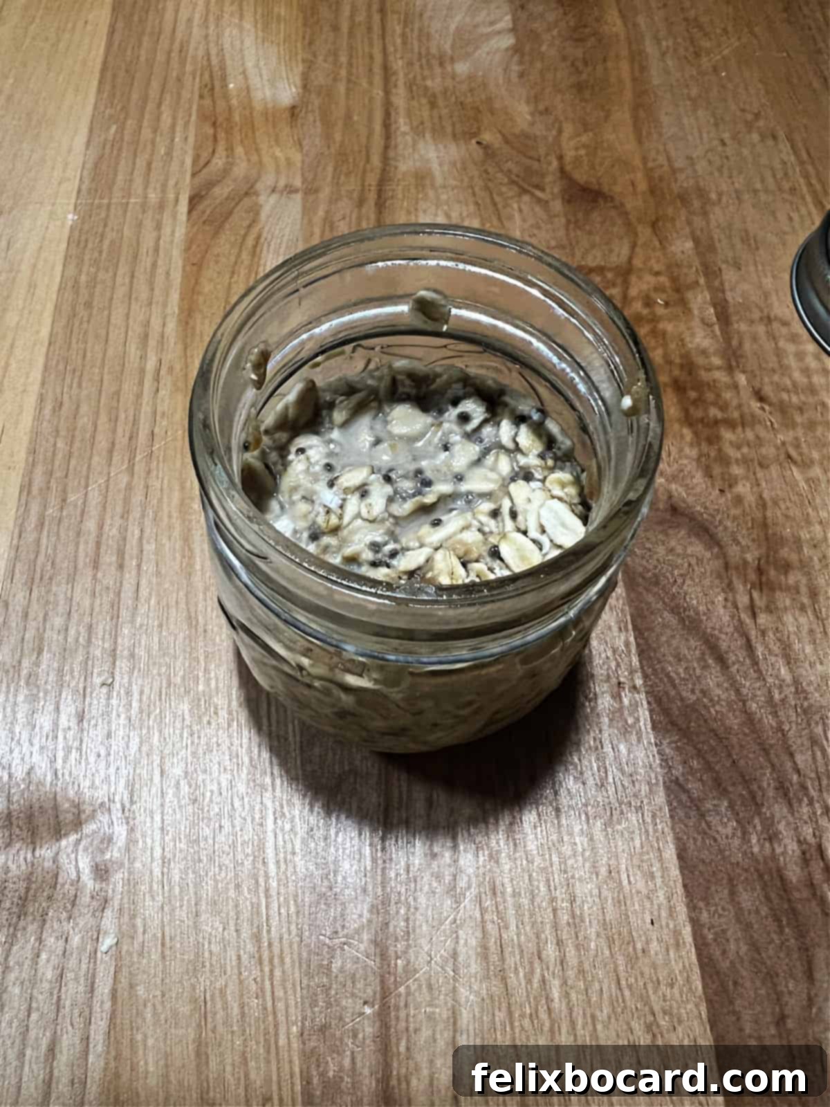 A glass jar filled with mixed peanut butter overnight oats ingredients, sealed with a lid and ready to be placed in the refrigerator for the night.