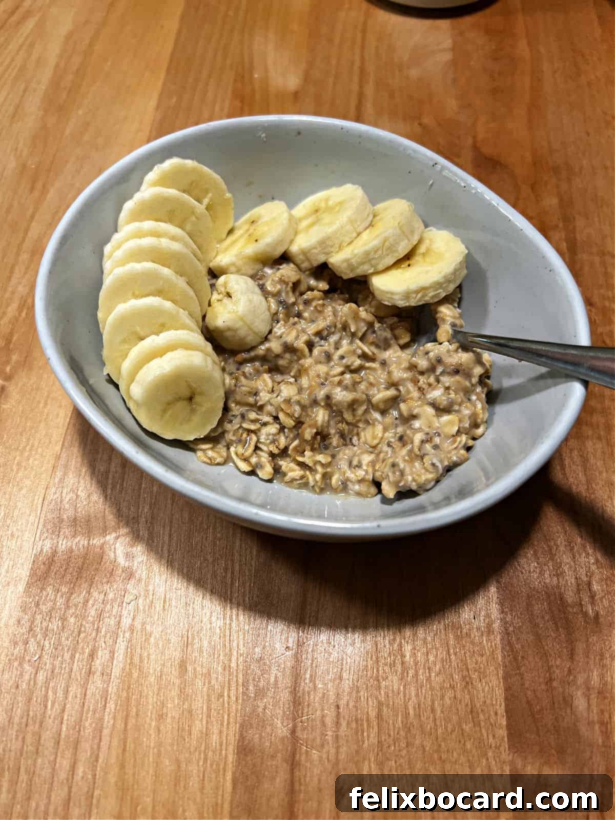 A bowl of creamy peanut butter overnight oats topped with beautifully fanned fresh banana slices, ready to be eaten for a healthy breakfast.