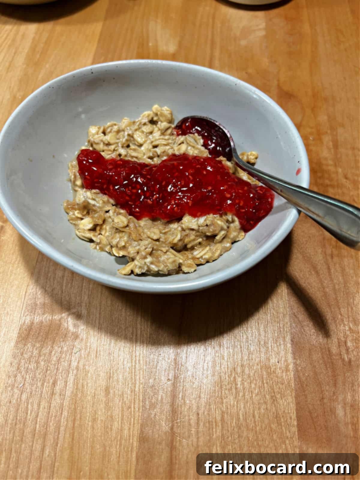 A bowl of creamy peanut butter overnight oats swirled with vibrant raspberry jam, evoking the classic PB&J sandwich in a healthy breakfast form.