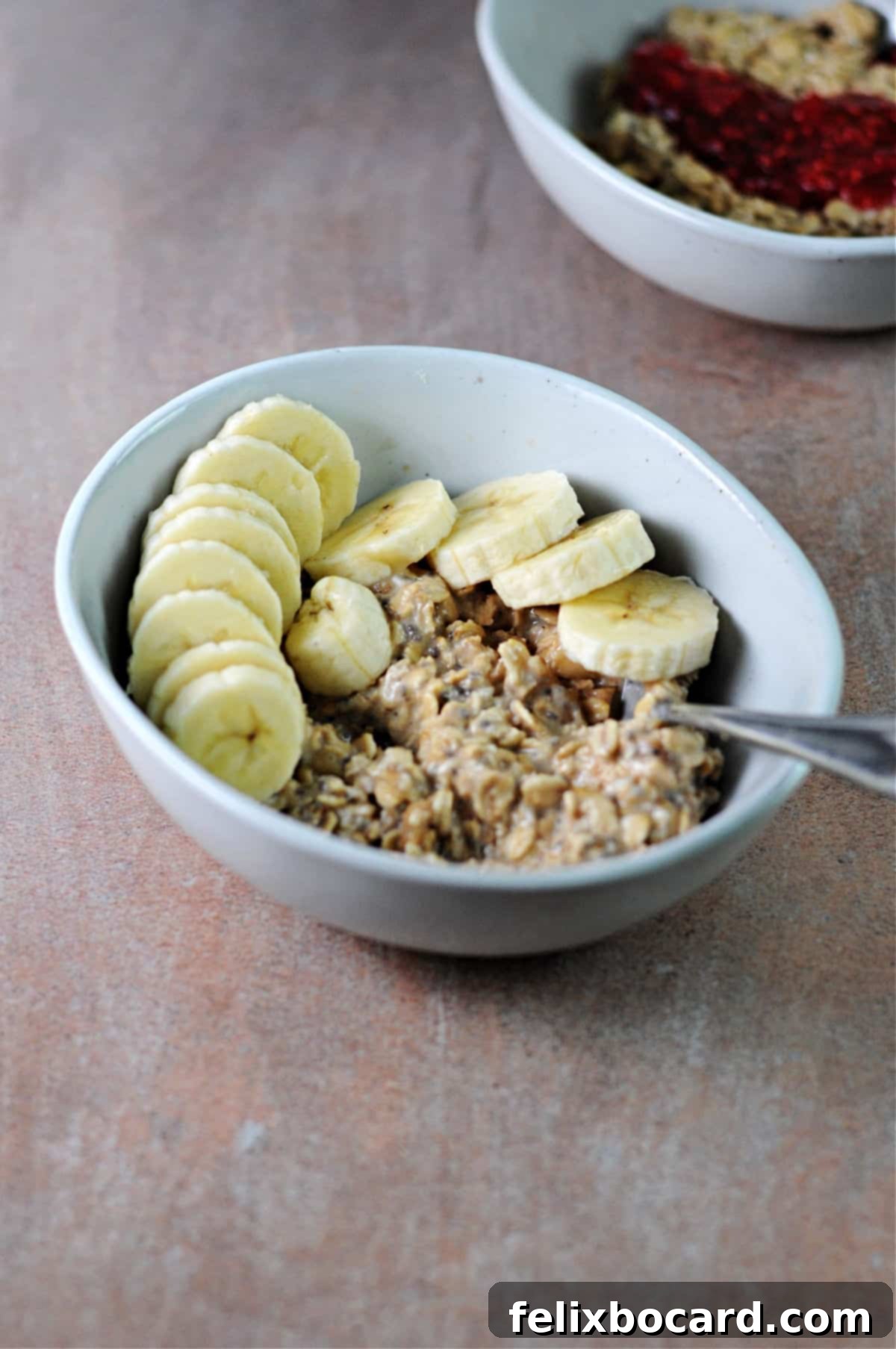 Two visually appealing bowls of peanut butter overnight oats, one topped with sliced banana and the other with a swirl of raspberry jam, showcasing diverse and delicious breakfast options.