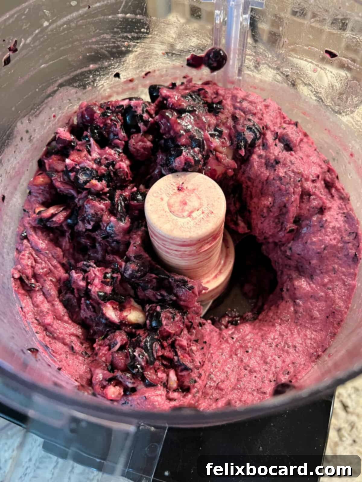 The food processor with partially processed blueberry nice cream, showing the initial, still-chunky texture before full creaminess is achieved.