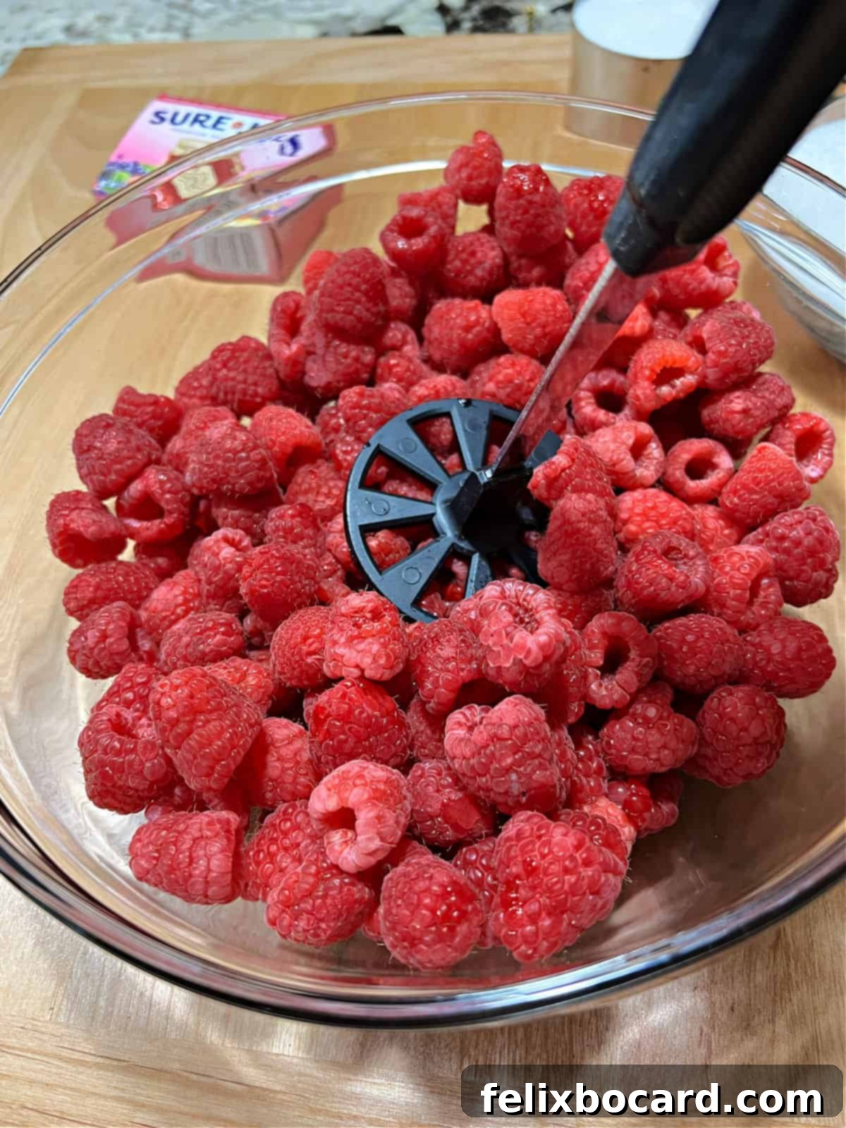 Homemade Reduced Sugar Raspberry Freezer Jam 5 potato masher starting to crush a large bowl of berries.