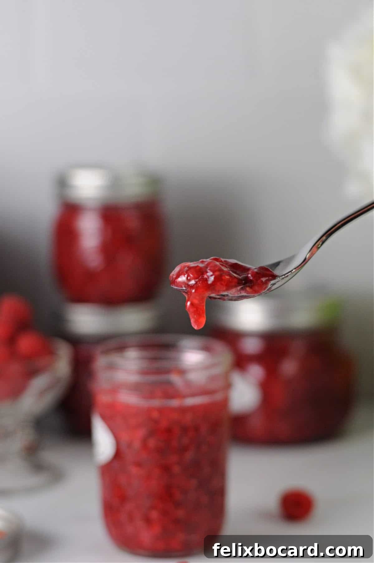 Homemade Reduced Sugar Raspberry Freezer Jam 8 spoonful of low sugar freezer jam with a small amount looking like it will drip off.
