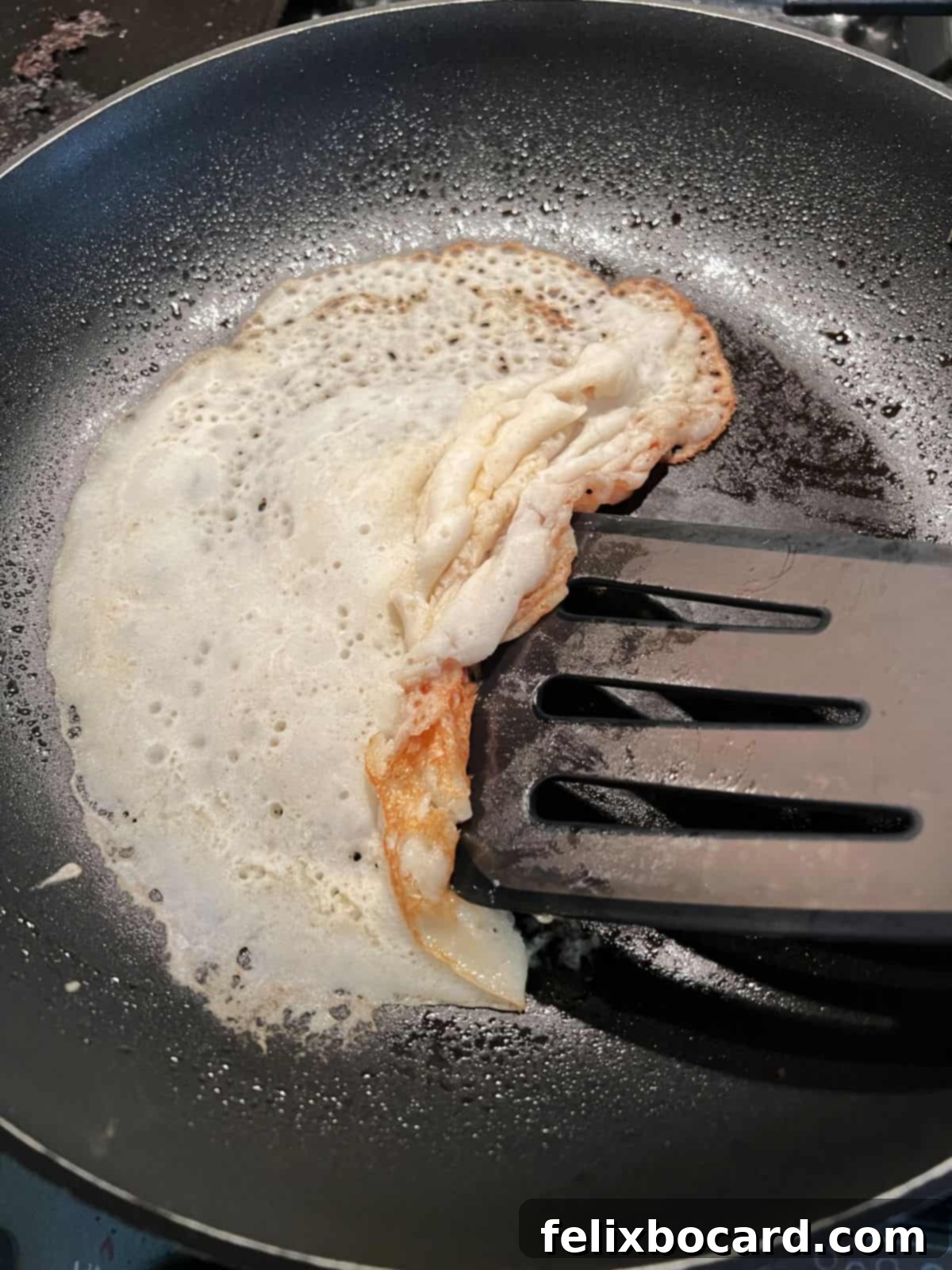 A crepe in a skillet, visibly folding and tearing as a spatula attempts to lift and flip it, illustrating a failed attempt.